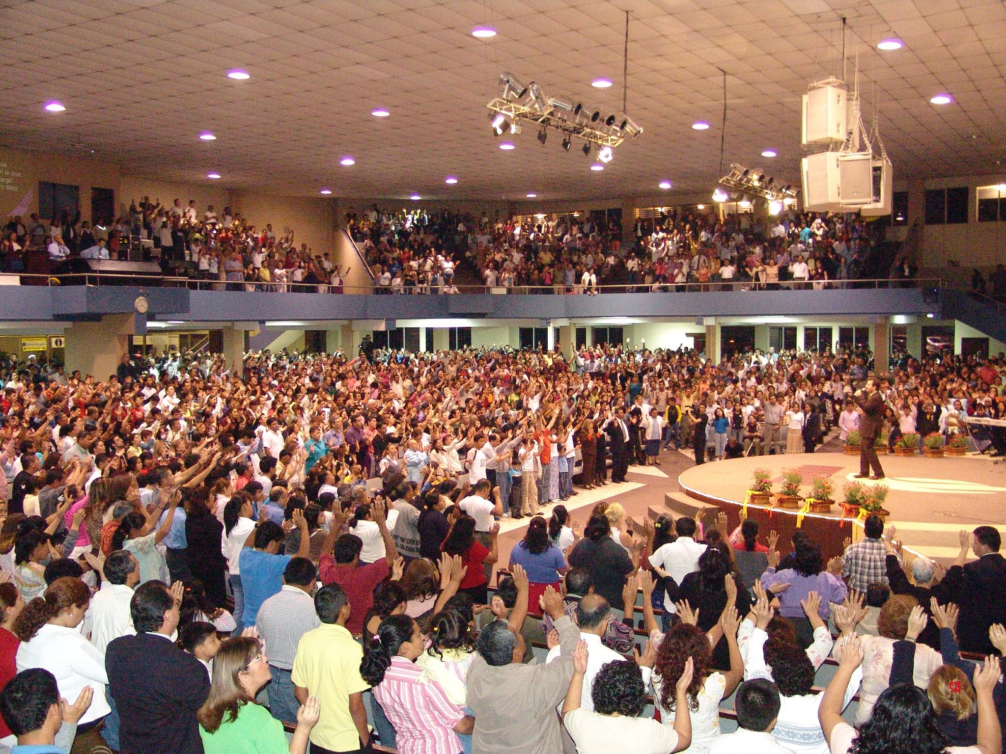 Vista de una gran congregación con las manos levantadas durante una reunión cristiana.
