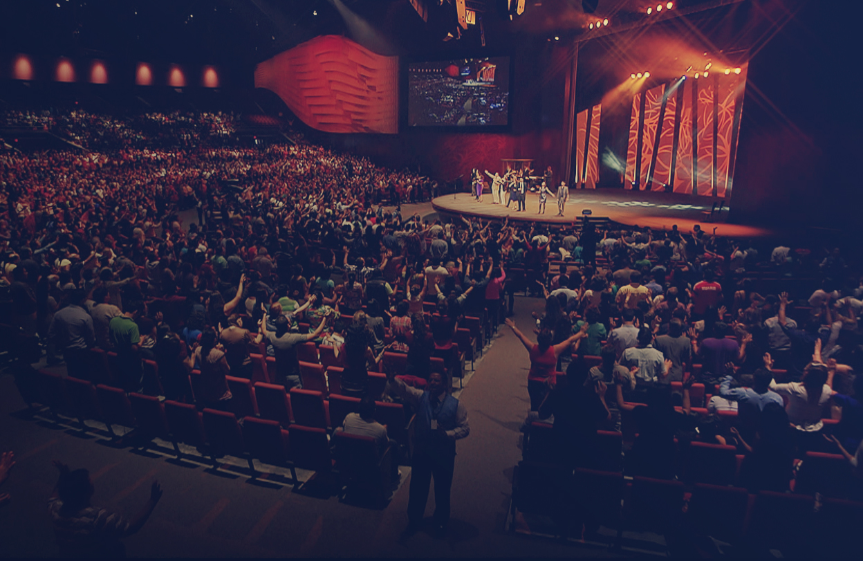 Vista amplia de un gran auditorio lleno durante una reunión cristiana con la congregación en adoración.