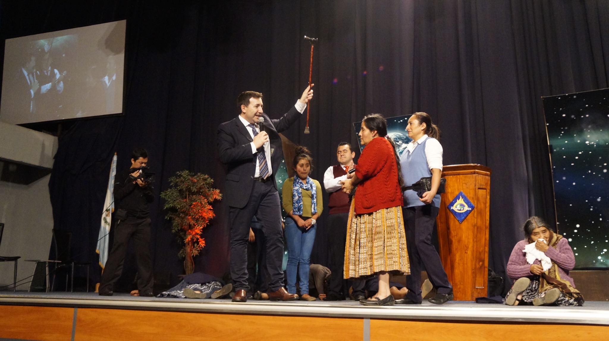 Manuel ministrando con micrófono mientras acompaña a varias personas sobre el escenario en una reunión cristiana.