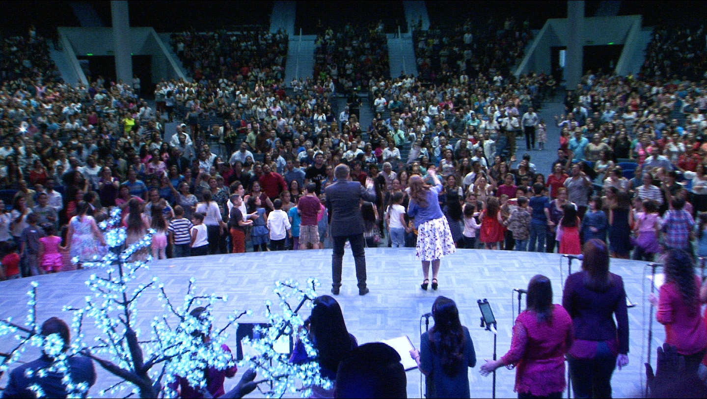 Vista desde el escenario hacia una gran congregación durante una reunión cristiana.